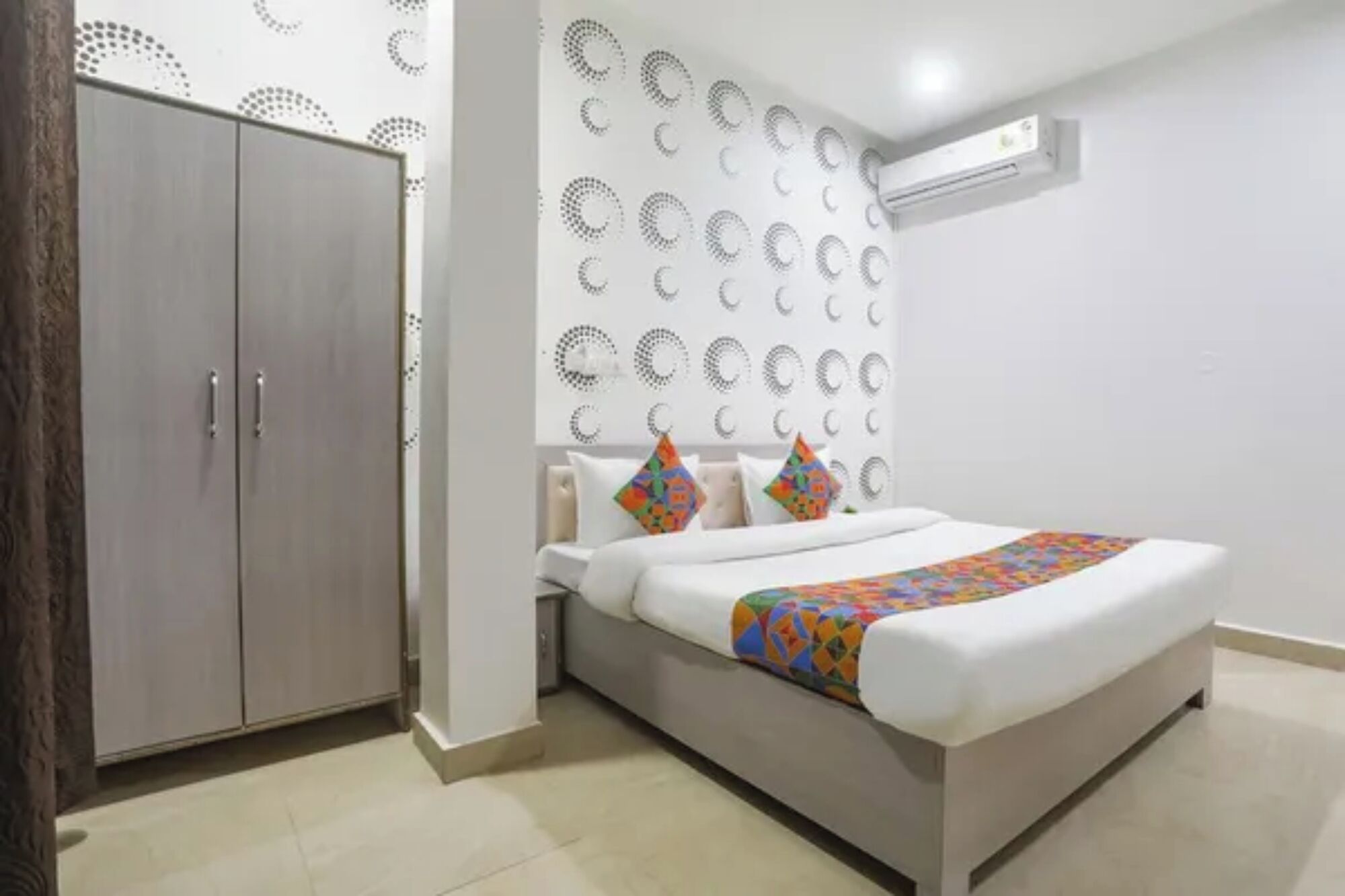 A bedroom with a bed, a wardrobe, a wall-mounted air conditioner, and a patterned wall.