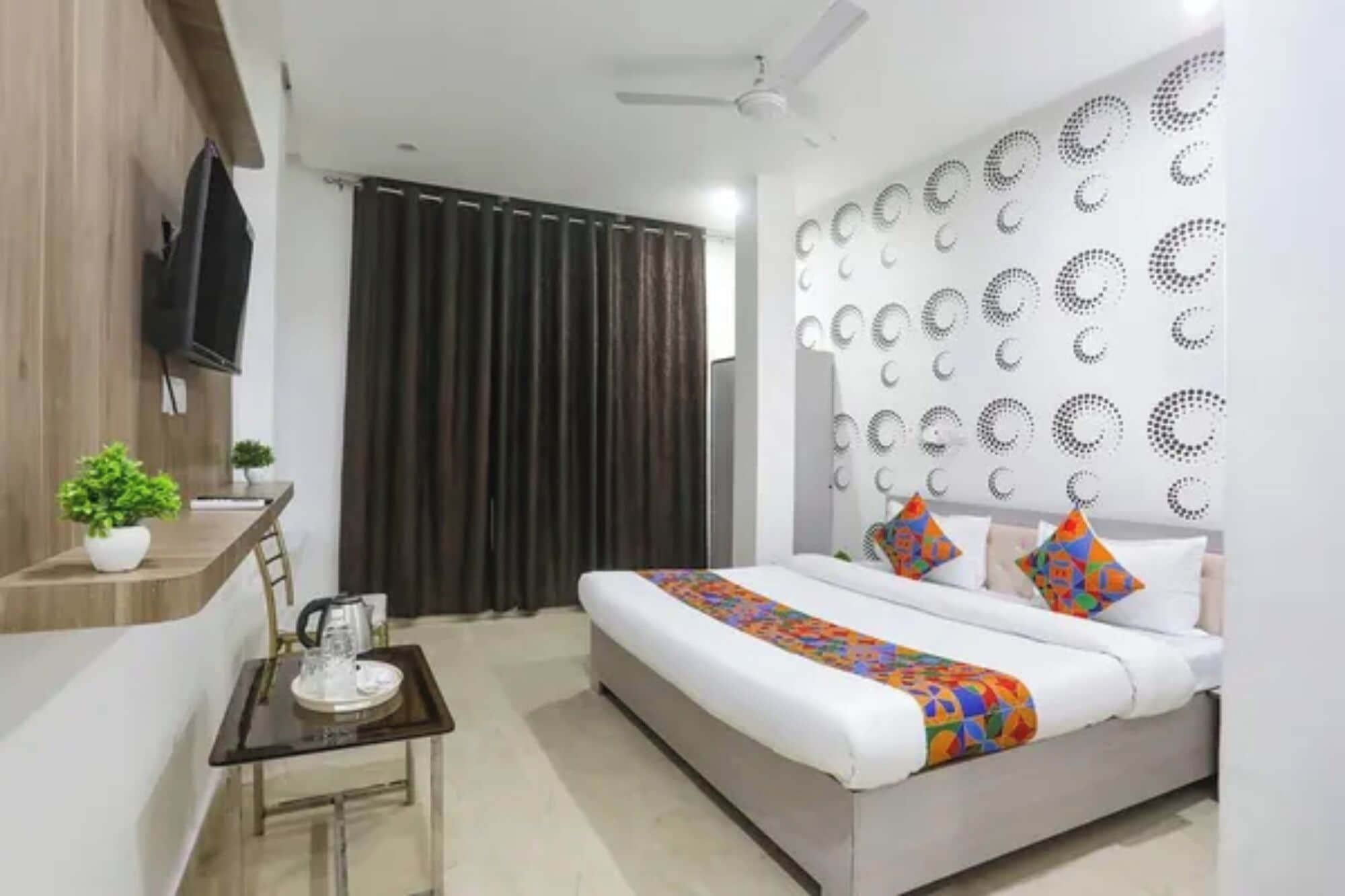 Habitación de hotel moderna con cama, una mesita con hervidor, una planta en maceta y una pared con diseños circulares.