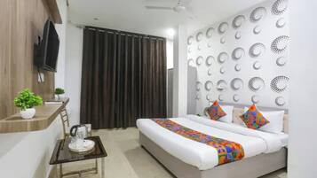 Habitación de hotel moderna con cama, una mesita con hervidor, una planta en maceta y una pared con diseños circulares.