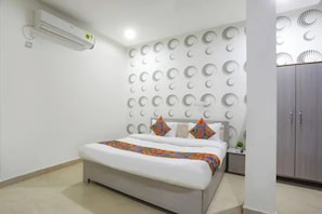 Una habitación de hotel con una cama, una mesita de noche, un equipo de aire acondicionado y un armario.