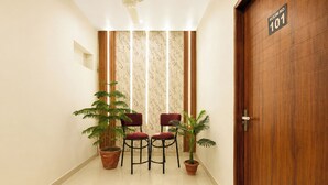 A hallway with a wooden door labeled 'ROOM NO 101,' two red chairs, and two potted plants. - Fabhotel Anand Palace (Jaipur)