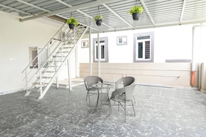 A covered outdoor area with a staircase, two wicker chairs, and hanging potted plants.
