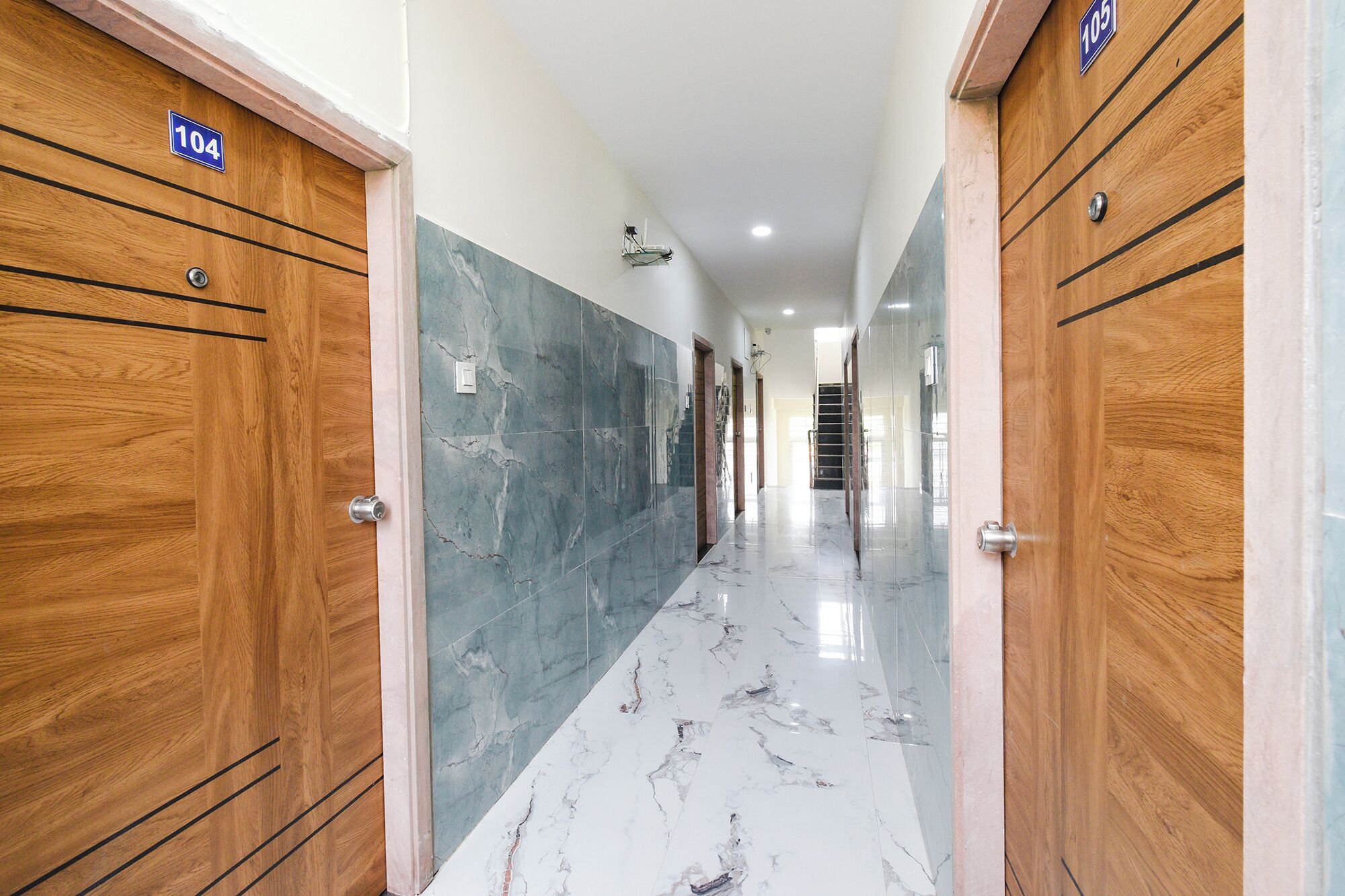 Un pasillo con puertas de madera, suelo de mármol y una escalera al fondo.