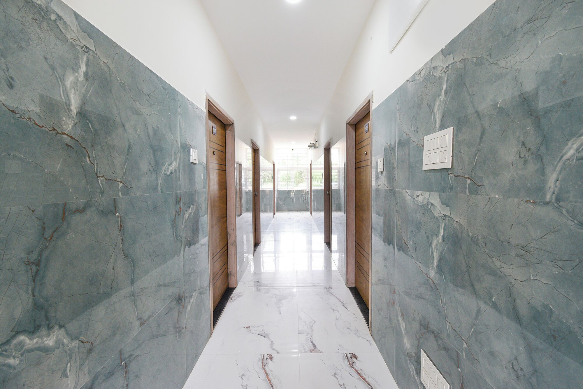 A hallway with marble walls and doors, leading to a bright room.