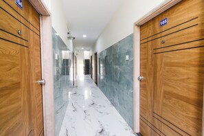 Un pasillo con suelo de mármol, puertas de madera y una lámpara en el techo.