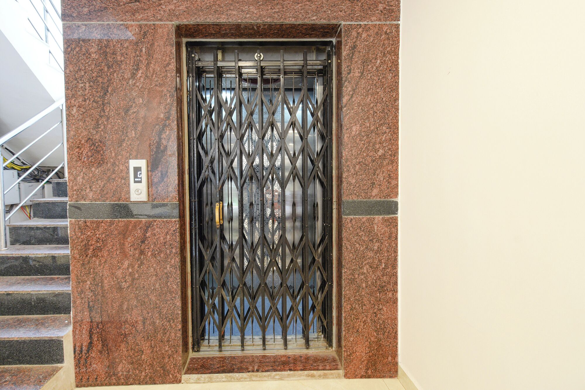 An elevator with a metal security gate, a marble wall, and a staircase to the left.