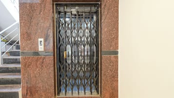 An elevator with a metal security gate, a marble wall, and a staircase to the left.
