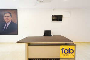 Un mostrador de recepción de hotel con un televisor de pantalla plana, un ventilador de techo y un retrato en la pared.