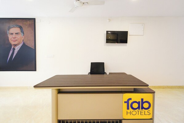 A hotel reception desk with a flat-screen TV, a ceiling fan, and a portrait on the wall.