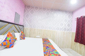A hotel room with a bed, pillows, a patterned wall, and a curtain.