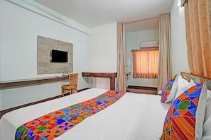 A hotel room with a bed, a desk, a chair, a television, and a bathroom visible through an open door. - FabHotel Skanda Inn (Tirupati)