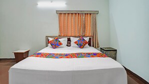 A hotel room with a bed, a nightstand, a wooden side table, and a window with curtains. - Fabhotel Skanda Inn (Tirupati)