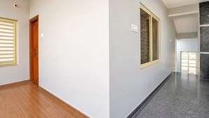 A hallway with wooden flooring, a wooden door, and a window with blinds. - Fabhotel Skanda Inn (Tirupati)
