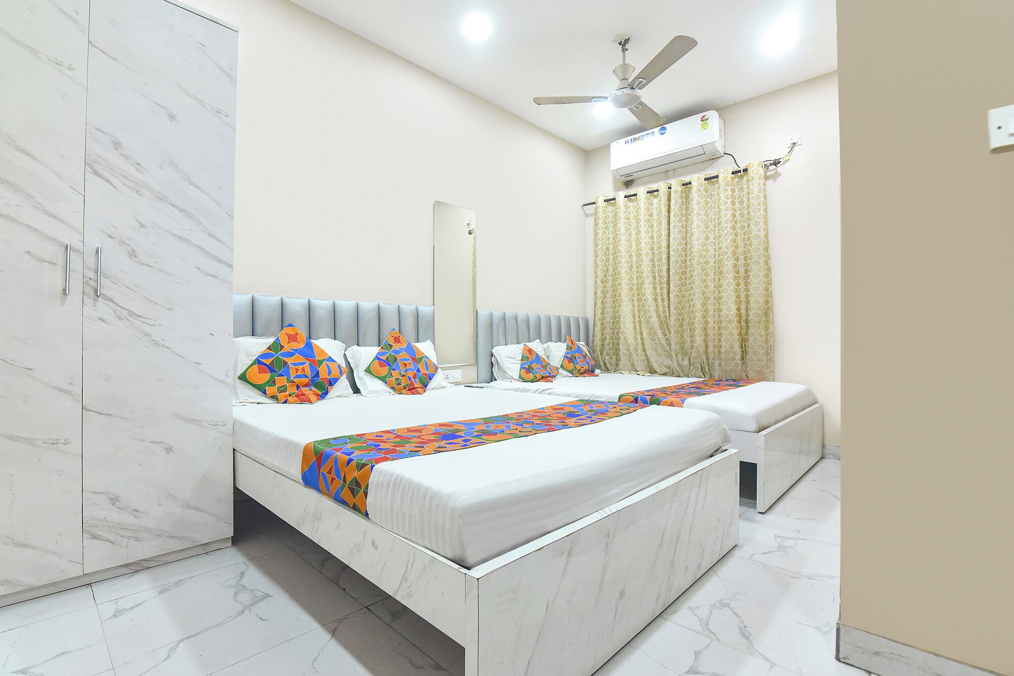 Quarto de hotel com cama, ventoinha no teto, aparelho de ar condicionado e banheiro com vaso sanitário.