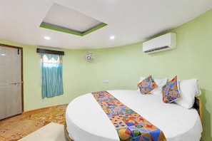 A hotel room with a bed, a ceiling fan, an air conditioning unit, and a window with curtains.