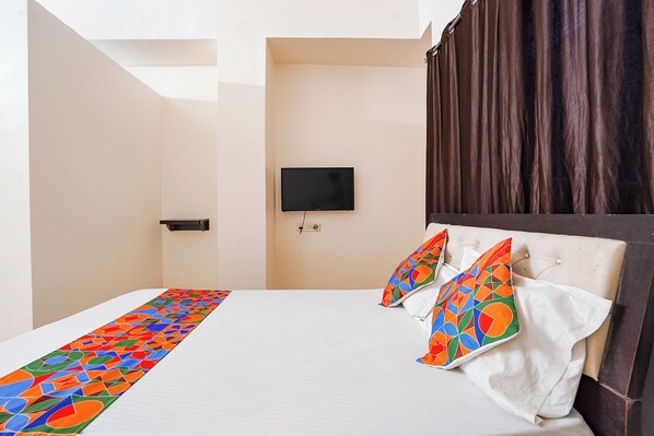 A hotel room with a bed, a television on the wall, and a window with curtains.