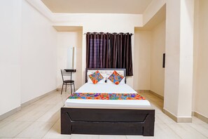 A bedroom with a bed, a chair, a mirror, and a window with curtains. - Via Royal Rest Rooms (Pune)