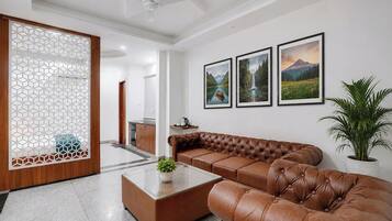 A modern living room with a leather sofa, a glass coffee table, and framed landscape paintings on the wall.