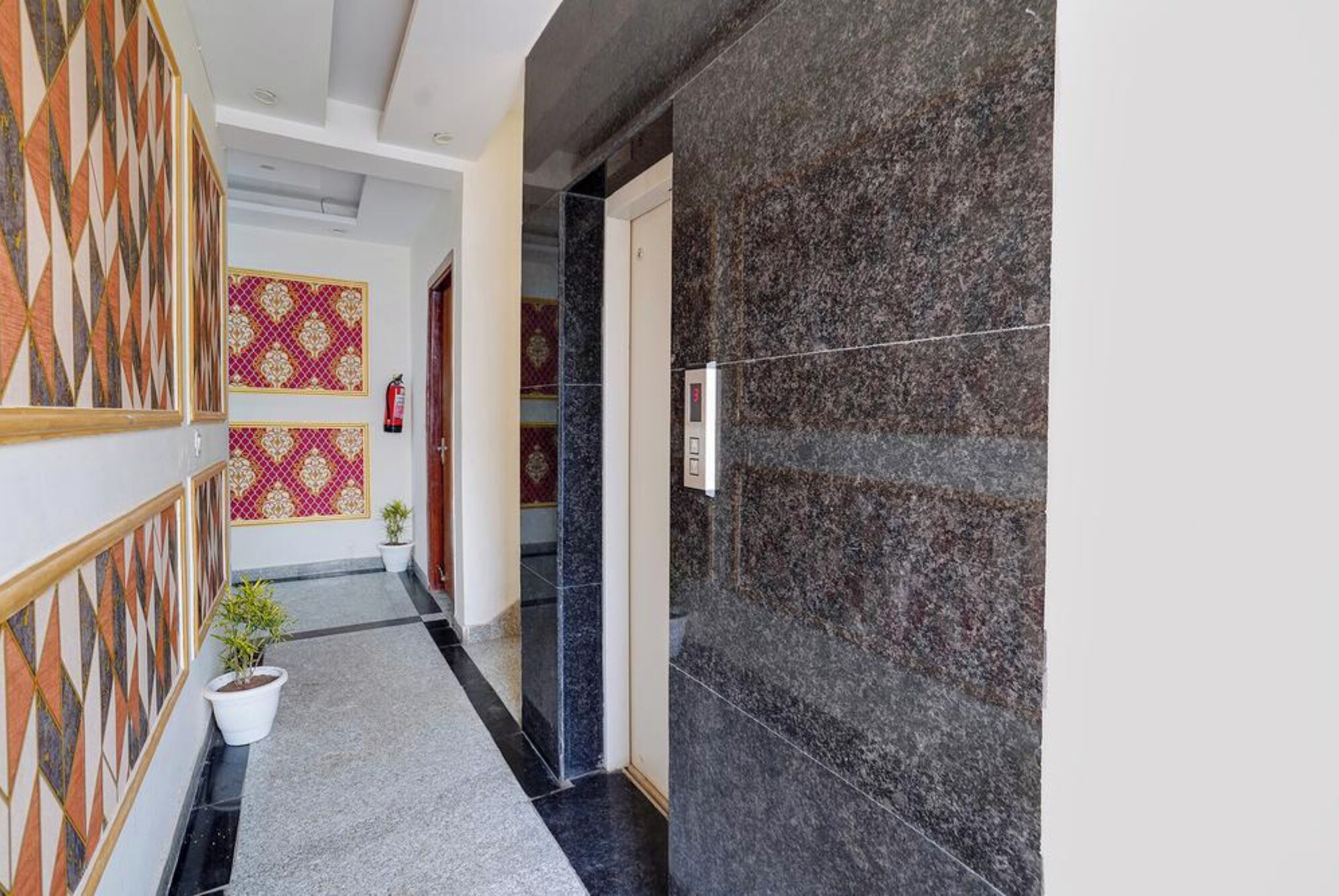 A hallway with patterned walls, a potted plant, and a fire extinguisher.