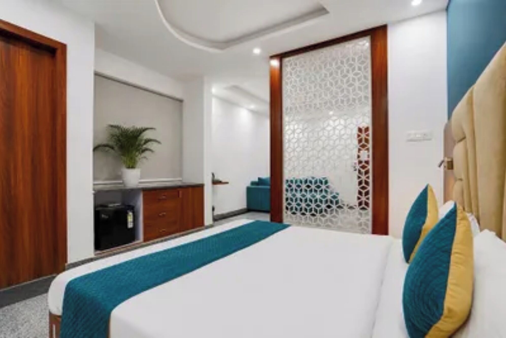 A hotel room with a bed, a desk, and a potted plant.