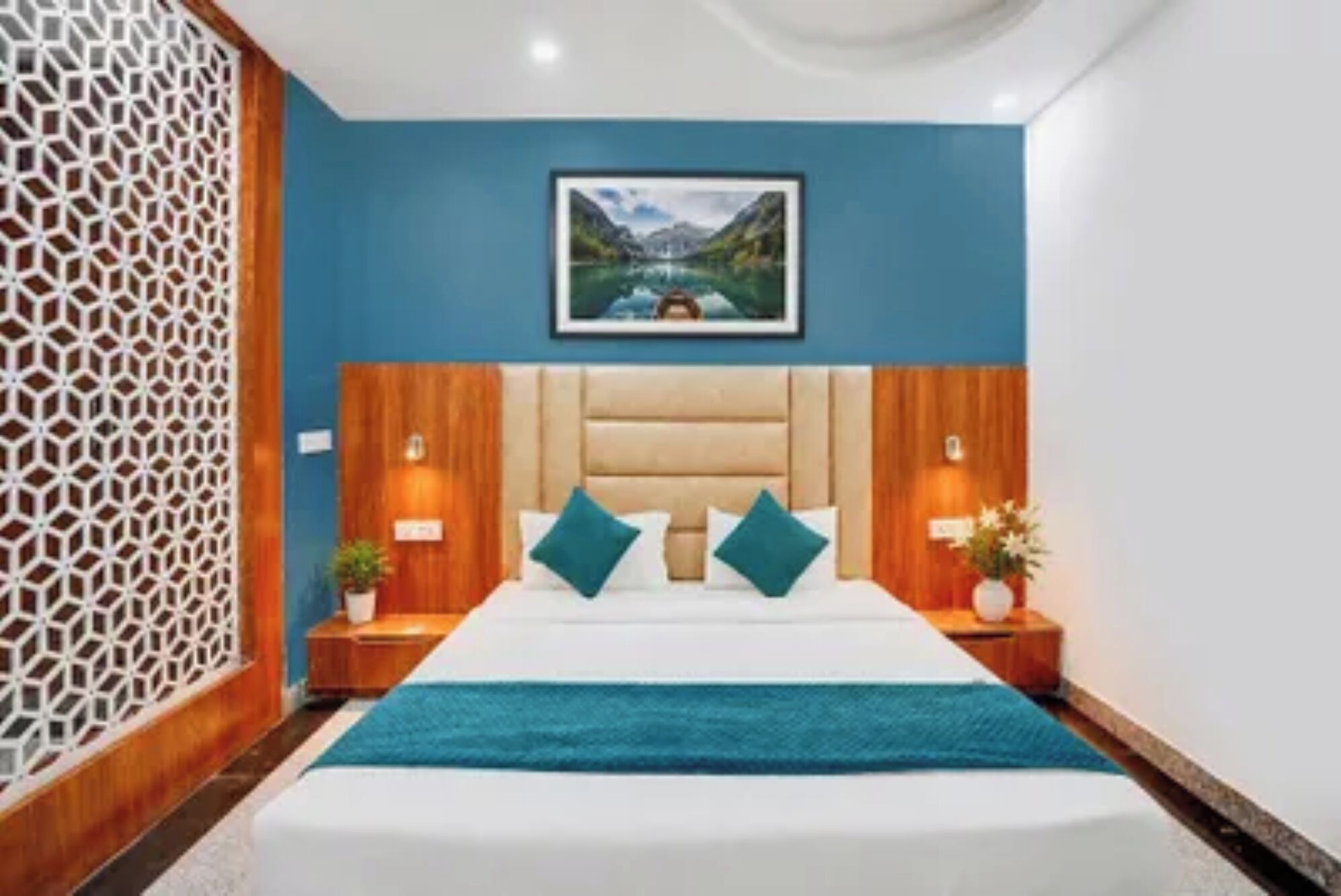 A bedroom with a bed, a headboard, two bedside tables, a nightstand, a wall-mounted picture, and a decorative wall panel.