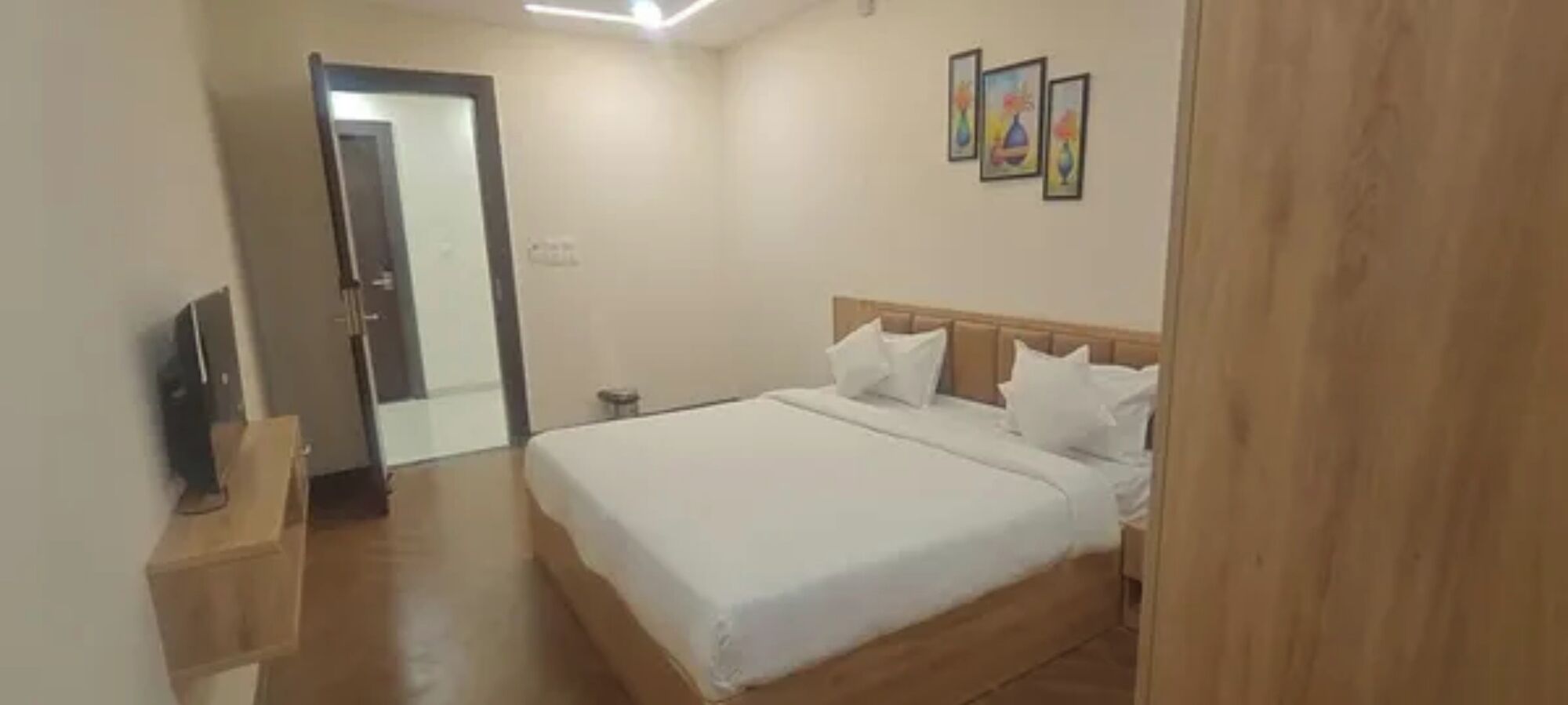 Une chambre d’hôtel avec un lit, un téléviseur posé sur un meuble, une porte et trois tableaux encadrés accrochés au mur.