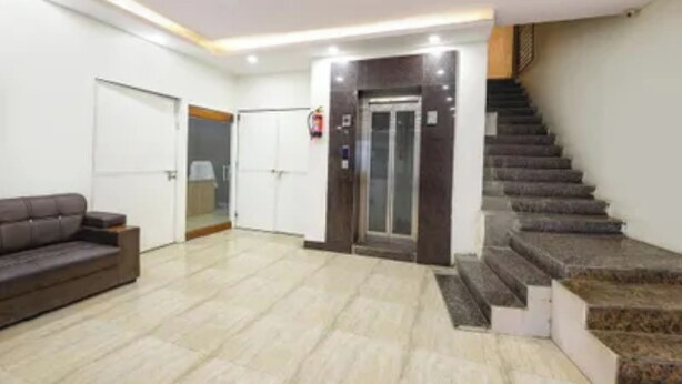 A spacious lobby with a staircase, a sofa, and a door leading to a room. - Via Lazeeno (Faridabad)