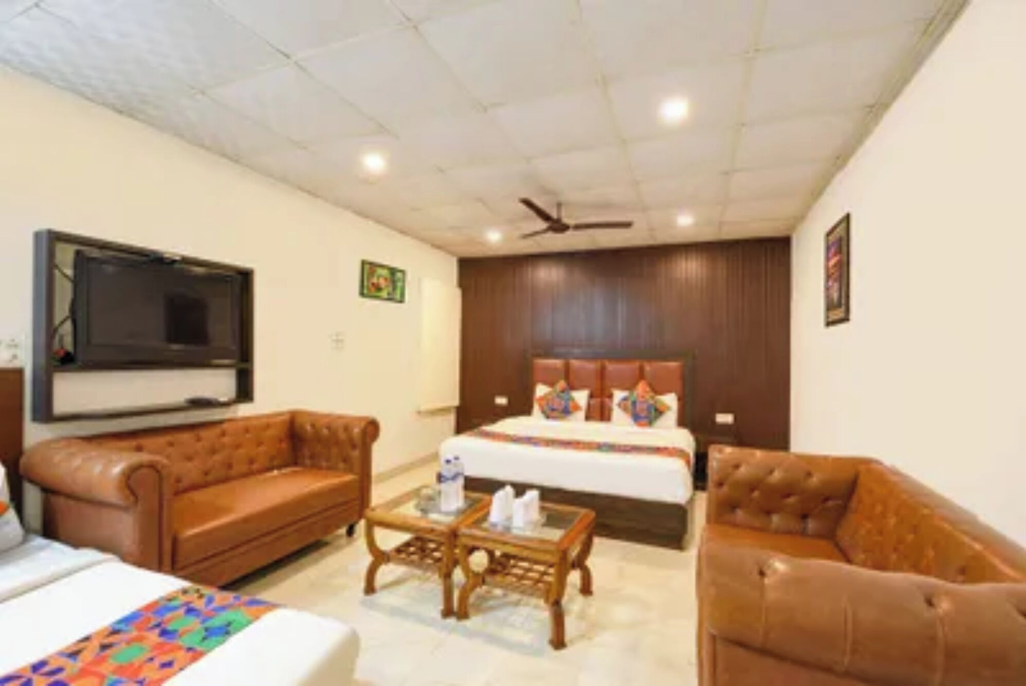 A hotel room with a bed, two sofas, a coffee table, a TV, and a ceiling fan.