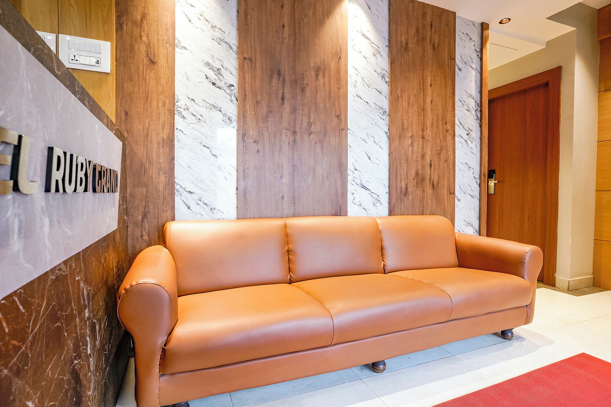 Un hall d’entrée moderne avec un canapé en cuir, un mur en marbre, des lambris en bois et une porte.