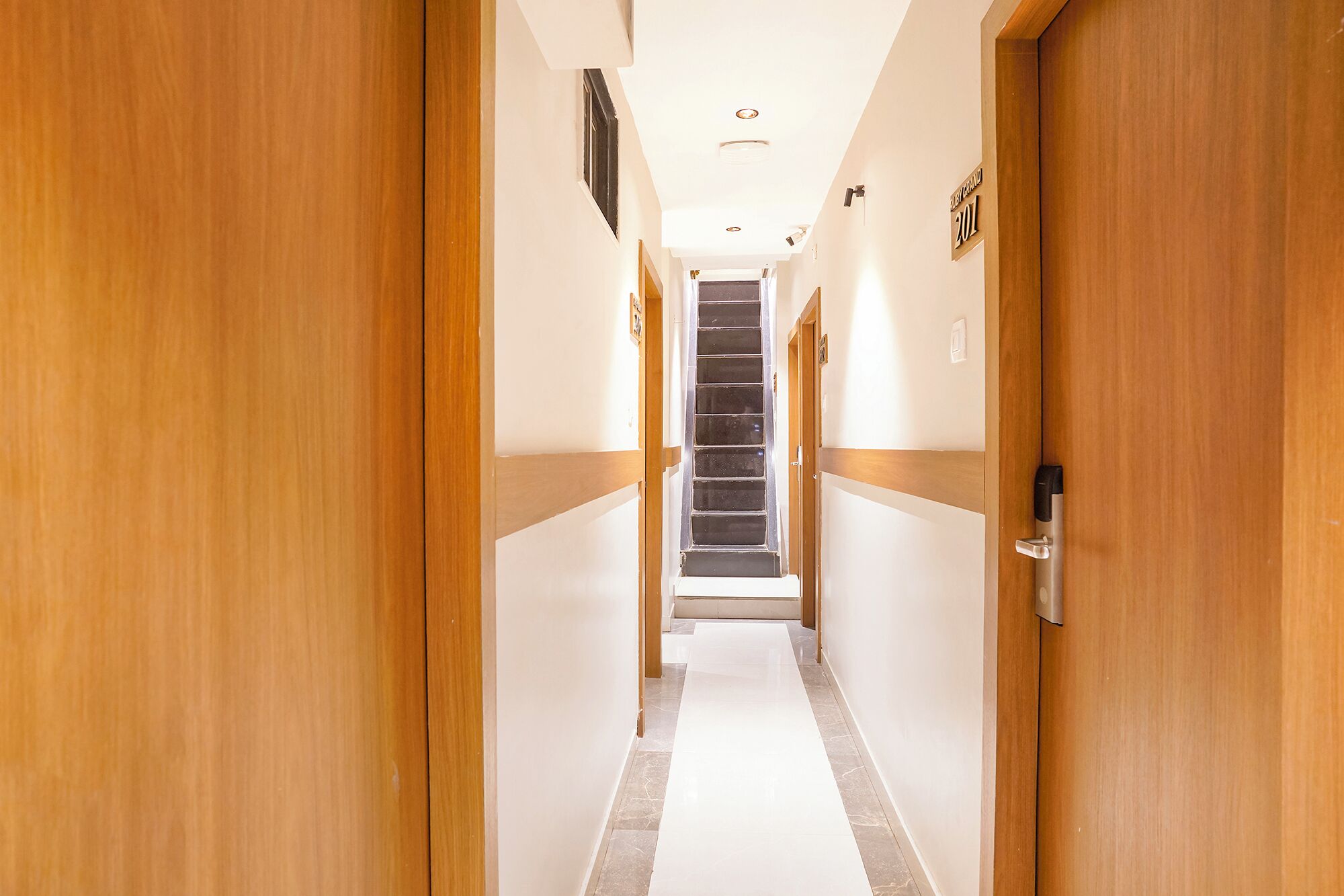 A hotel hallway with wooden doors, a tiled floor, and a staircase leading to an upper level.