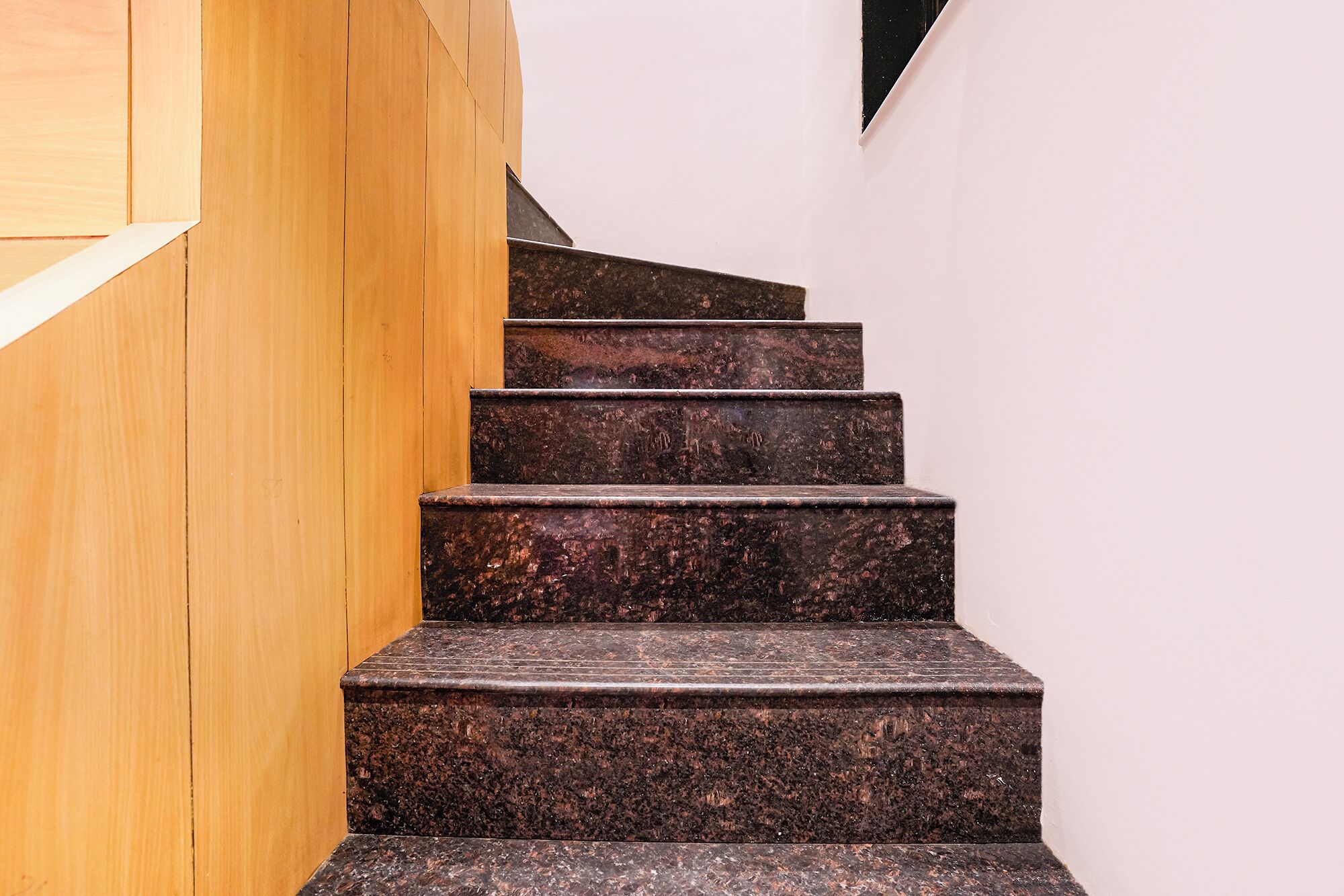 A staircase with a wooden handrail and dark granite steps.