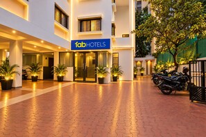 Entrada de hotel con un letrero que dice 'fab hotels', plantas en macetas y un camino pavimentado.