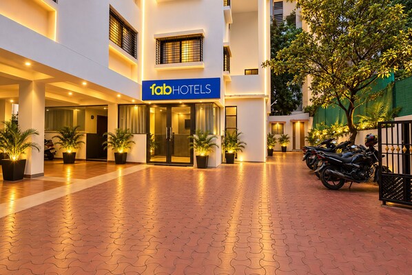 Entrada de hotel con un letrero que dice 'fab hotels', plantas en macetas y un camino pavimentado.