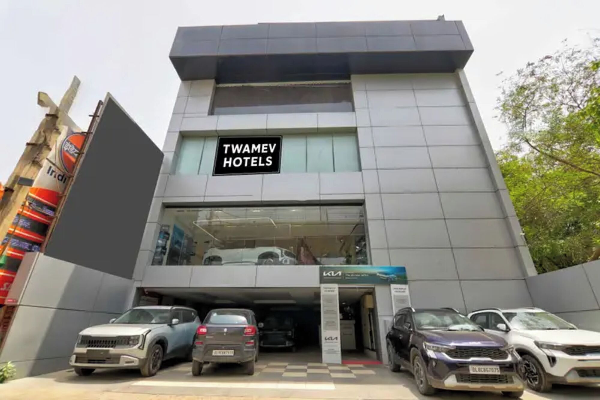 A modern building with a sign for Twamev Hotels. There are several cars parked in front.