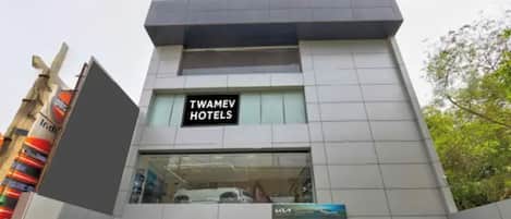 Un edificio moderno con un cartel de Twamev Hotels. Varias coches estacionados adelante.