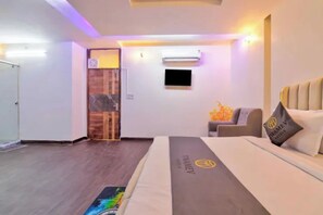 Quarto de hotel com cama, sofá, televisão e porta.