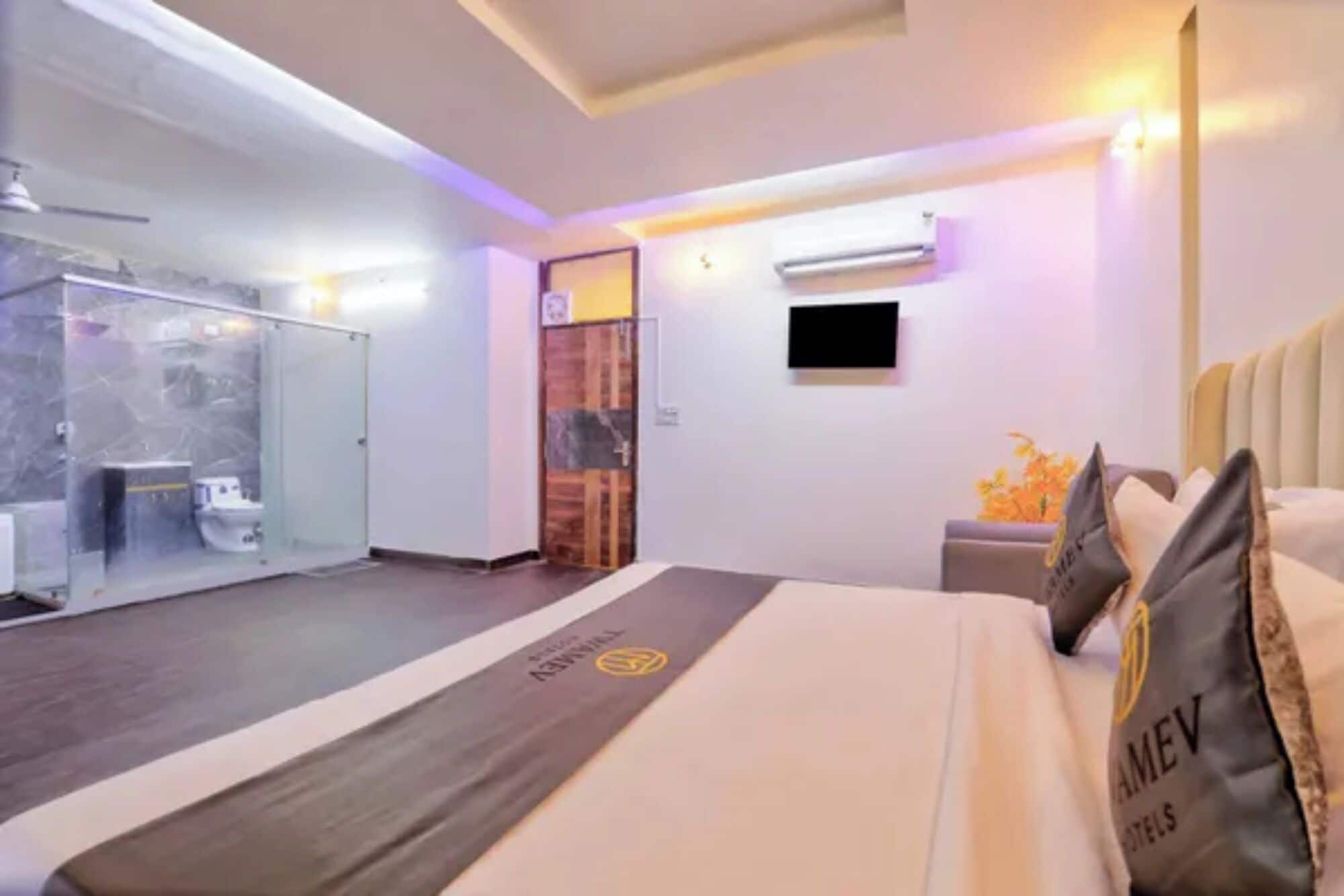 A modern hotel room with a large bed, a glass-enclosed bathroom, and a flat-screen TV mounted on the wall.