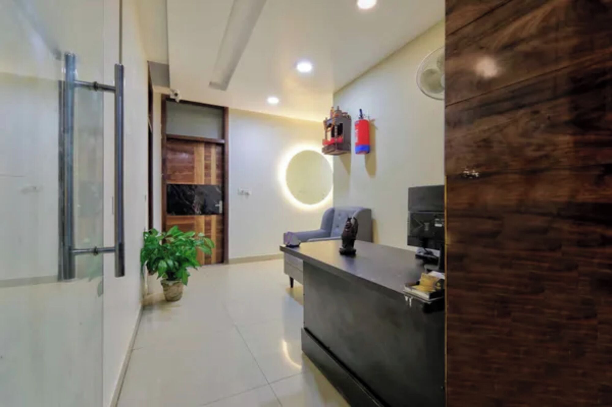 A reception area with a desk, a potted plant, a circular light fixture, and a fire extinguisher.