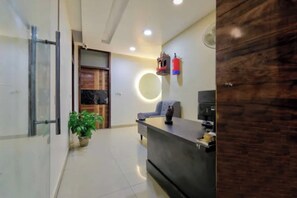 Uma área de recepção com balcão, planta em vaso, luminária circular e extintor de incêndio.