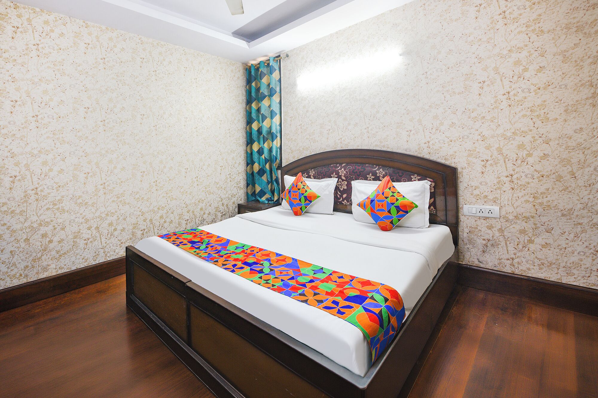 Uma cama bem arrumada com colcha estampada e duas almofadas decorativas, cabeceira de madeira e parede com papel de parede floral.