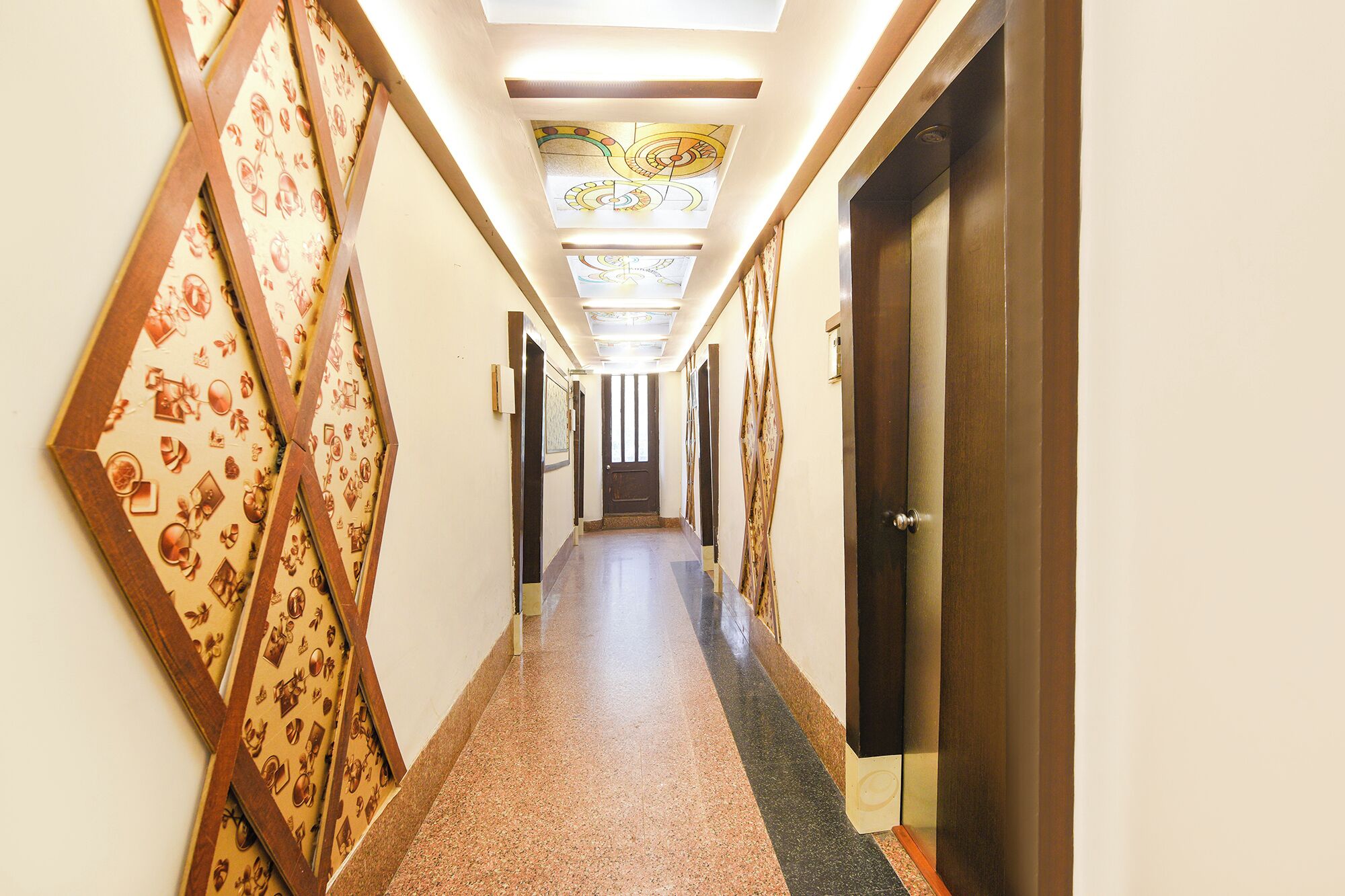 A hotel corridor with patterned wallpaper, a tiled floor, and a ceiling with a geometric design.