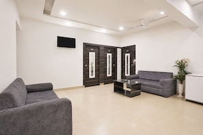 A modern waiting area with a sofa, a coffee table, and a reception desk. - Fabhotel Mid Way (Gandhinagar)
