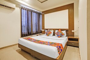 A hotel room with a bed, a nightstand, a mirror, and a window with curtains. - FabHotel Mid Way (Gandhinagar)