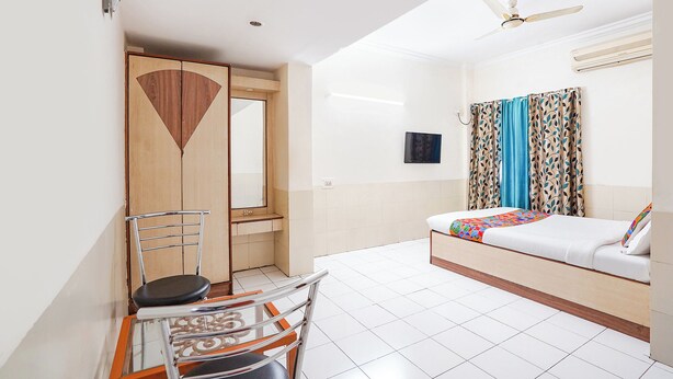 Habitación de hotel con cama, escritorio con silla, armario, ventilador de techo y televisor.