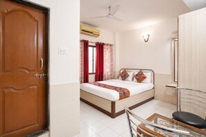 A hotel room with a wooden door, a bed with patterned pillows, a ceiling fan, and a tiled floor. - FabHotel Gandharva Inn (Pune)