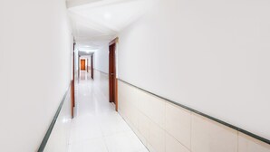 Un pasillo largo y estrecho con paredes blancas y un piso brillante, que conduce a una puerta al final.