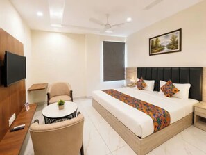 A hotel room with a bed, a television, a chair, a small table with a plant, and a painting on the wall. - FabHotel K9 Regency (Zirakpur)