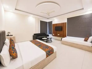 Habitación de hotel moderna con una cama grande, un sofá, una mesita y un televisor montado en la pared.