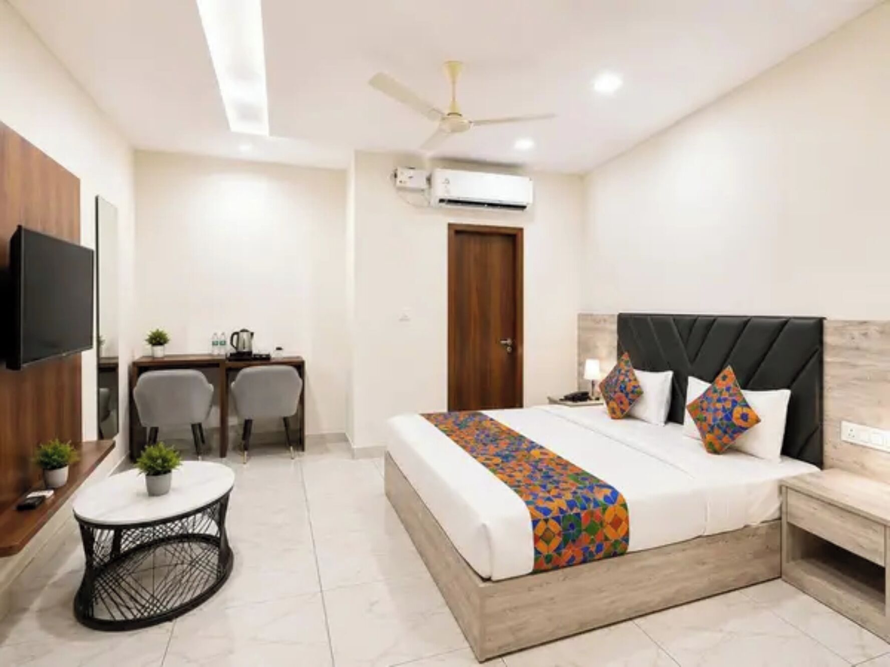 A hotel room with a bed, a desk, a chair, a TV, and a ceiling fan.