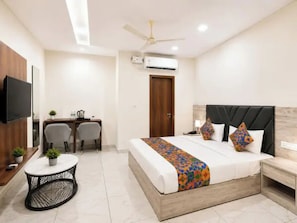 Habitación de hotel con cama, escritorio, silla, televisor y ventilador de techo.